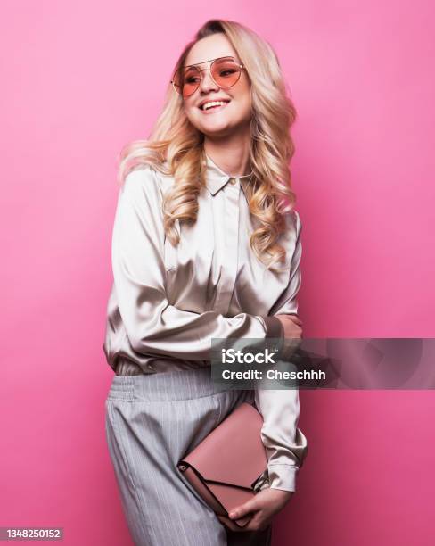 Young Beautiful Blond Woman Wearing Blouse Pants And Sunglasses Holds A Handbag And Posing On A Pink Background Stock Photo - Download Image Now