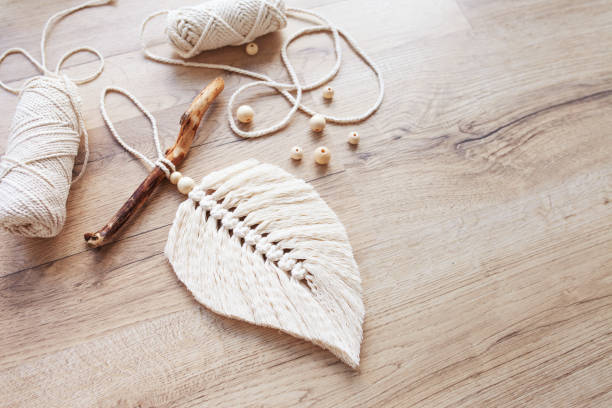 Macrame leaf  in natural color and thread windings lying on a wooden table. Cotton rope decor macrame to make your room more cozy and unique. Woman hobby. Handmade wall hanging decor.