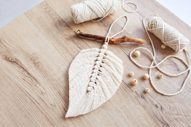 istock Macrame leaf  in natural color and thread windings lying on a wooden table. Cotton rope decor macrame to make your room more cozy and unique. Woman hobby. Handmade wall hanging decor. Copy space 1348252324