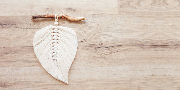 istock Macrame leaf  in natural color and thread windings lying on a wooden table. Cotton rope decor macrame to make your room more cozy and unique. Woman hobby. Handmade wall hanging decor. Copy space. Banner 1348252338
