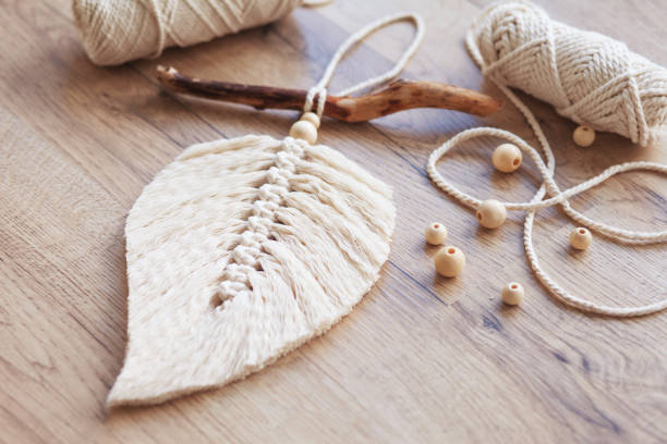Macrame leaf  in natural color and thread windings lying on a wooden table. Cotton rope decor macrame to make your room more cozy and unique. Woman hobby. Handmade wall hanging decor.