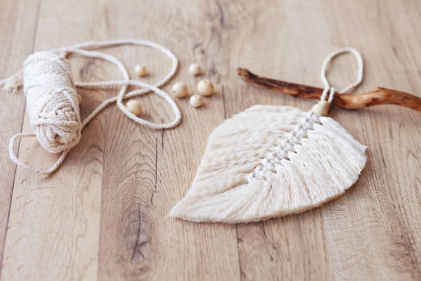 istock Macrame leaf  in natural color and thread windings lying on a wooden table. Cotton rope decor macrame to make your room more cozy and unique. Woman hobby. Handmade wall hanging decor. 1348252401