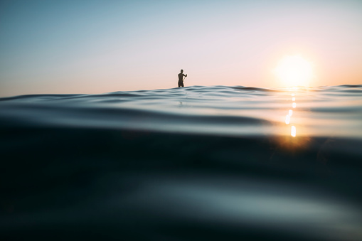 Low angle view of man paddleboarding on the sunset sea.