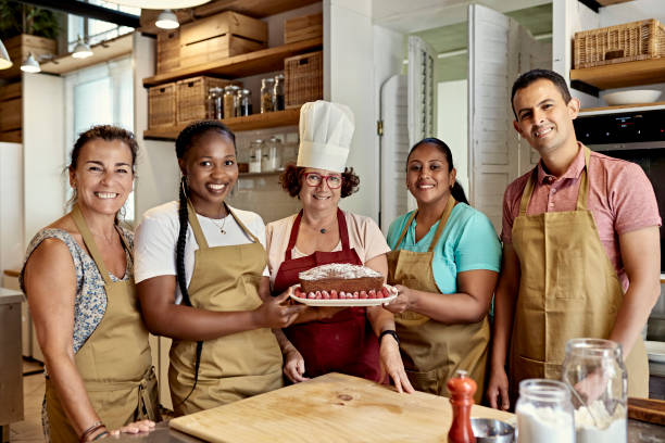 Portrait of Chef and Adult Students with Raspberry Cake Waist-up view of diverse group of corporate colleagues in aprons holding dessert and smiling at camera as they participate in team cooking event. north african ethnicity stock pictures, royalty-free photos & images
