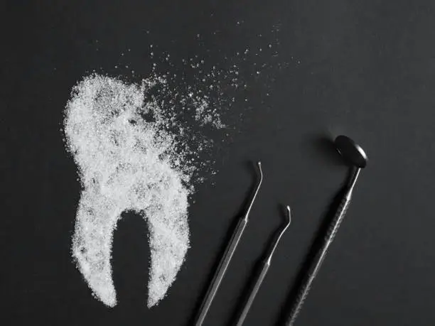 Sugar harms the tooth enamel. Image of a destroyed sugar tooth with medical instruments on a black background. Concept of dental medicine.