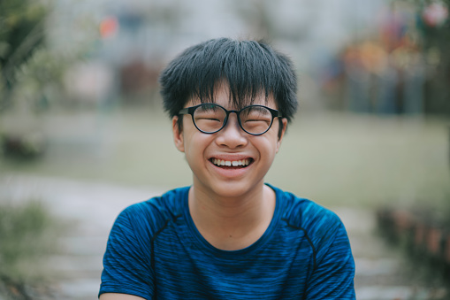 asian chinese teenage boy with eyeglasses looking at camera smiling at backyard of house outdoor