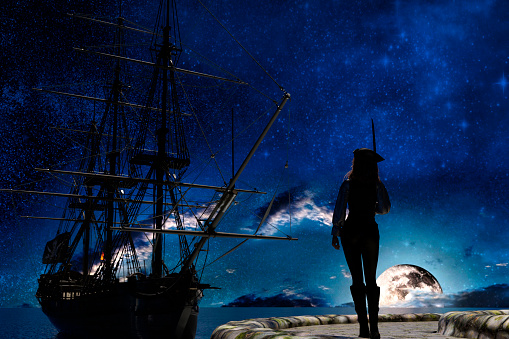 Mujer pirata observando el velero pirata a la luz de la luna photo