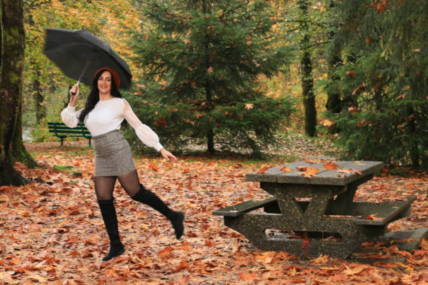 Autumn A woman happy to be in a public park in autumn. She is wearing a white shirt, gray mini skirt, black boots and umbrella, older women short skirts stock pictures, royalty-free photos & images