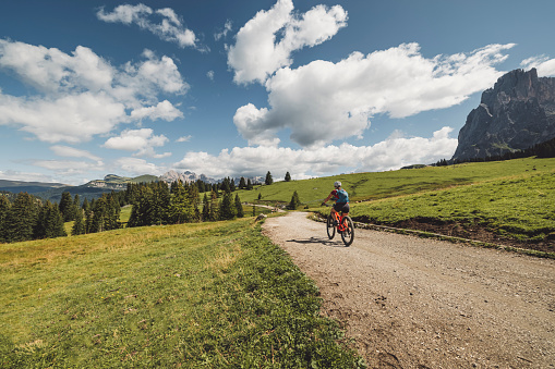 Back view of adventurous female exploring Dolomites on mountain bike. Riding on trails trough Alpe di Siusi, Seiser Alm, Val Gardena.