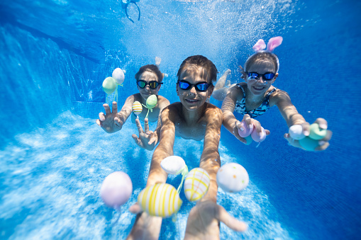 Summer Easter in swimming pool. Kids are playing in water and having fun with Easter eggs.\nCanon R5