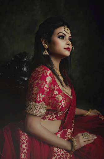 Most beautiful young lady with traditional ethnic red lehenga and jewellery sitting on a chair and celebrate Indian traditional festival diwali and durga puja