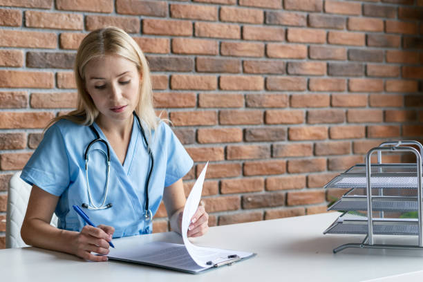 qualifizierte krankenschwester in blauen medizinischen uniform-ablagepapieren - document healthcare and medicine stethoscope history stock-fotos und bilder