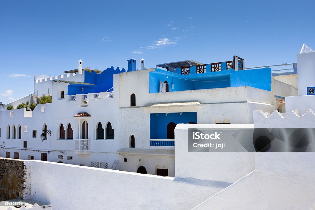 White and Blue Architecture, Asilah, Morocco White and blue stucco homes with a sea wall on a blue sky day in Asilah, Morocco. Asilah Stock Photo
