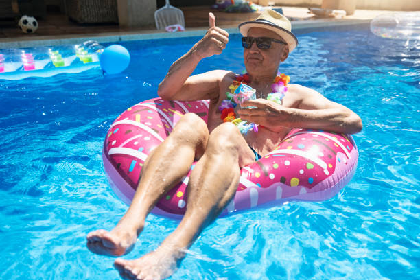 idoso curtindo relaxar na piscina - floating on water swimming pool men water - fotografias e filmes do acervo