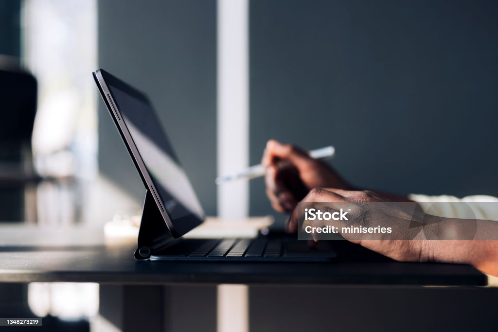 An Anonymous Business Woman Having Conference Call Meeting on Digital Tablet in a Cafe Unrecognizable African-American business woman typing notes on a keyboard while having online web conference on a digital tablet in a restaurant Web Conference Stock Photo