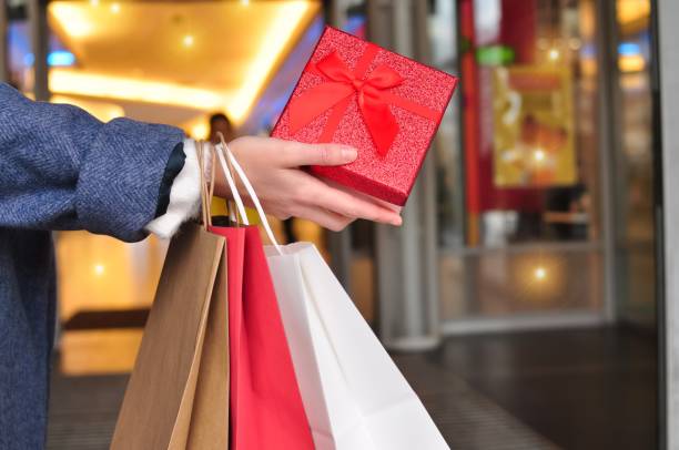 customer's hand holding shopping bag customer's hand holding red and white shopping bags in mall,copy space holiday shopping stock pictures, royalty-free photos & images