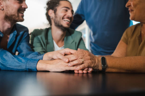 Young gay engaged couple coming out to parents - all smiling family members are not sitting at the table and lovingly holding hands. stock photo