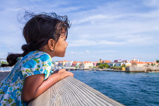 Little girl looking out to sea and in the background the coast of Willemstad, Curacao