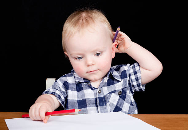 Young boy sitting at desk with pencils drawing stock photo