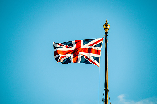 Hamilton, Bermuda: Bermudian flag against blue sky - The flag of the British Overseas Territory of Bermuda as a red ensign was first adopted in 1910. It is a British Red Ensign with the Union Flag (Union Jack) in the upper left corner, and the coat of arms of Bermuda in the lower right. The coat of arms of Bermuda displays a red lion holding a shield that has a depiction of a wrecked ship upon it. The red lion is a symbol of Great Britain. The wrecked ship is the Sea Venture, a 17th-century English sailing ship, part of the Third Supply mission to the Jamestown Colony, that was wrecked in Bermuda in 1609.