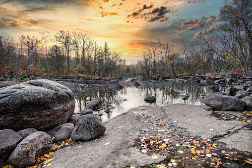 Grand Rapids Minnesota sunset over water. Large rocks and autumn leaves on shoreline. Outdoor scenic landscape