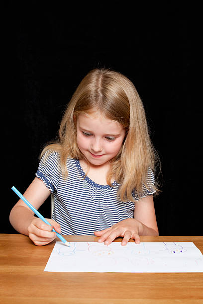 Young girl sitting at desk drawing a picture, Black Background stock photo