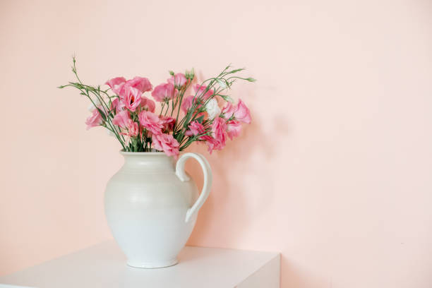 istock Bouquet with eustoma, summer flowers in a white vase, on a pink-beige background. 1348291447