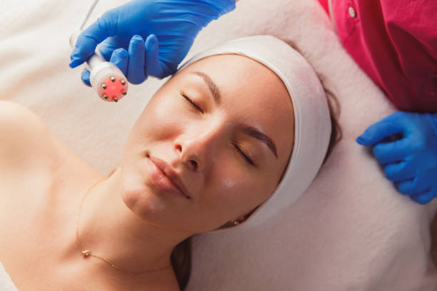 Facial Beauty Treatment. Woman Doing Red Led Light Therapy stock photo