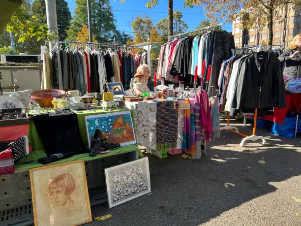 bancarella del mercato delle pulci con vestiti di seconda mano. nel mezzo c'è un'anziana signora seduta e in attesa dei clienti. - mercato delle pulci foto e immagini stock