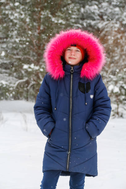 ritratto verticale di ragazza preadolescente in cappuccio caldo rosa brillante all'esterno sullo sfondo della foresta innevata invernale della natura. bel bambino che sorride all'aperto, freddo. bambino caucasico 10 anni. buone vacanze - 10 11 years cheerful happiness fun foto e immagini stock