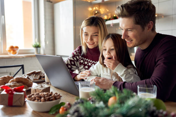 glückliche junge eltern mit süßen aufgeregten kleinen kleinen kleinen tochter mit laptop-computer zu hause sitzen am weihnachtstisch mit virtueller party auf videoanruf, e-commerce-familie online-shopping zusammen. - christmas shopping internet family stock-fotos und bilder