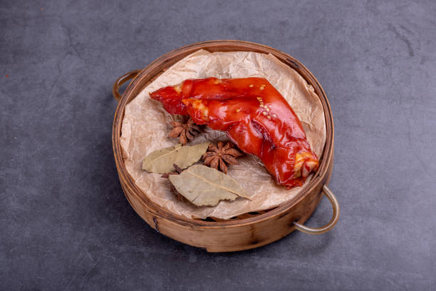 Stewed red pig's feet are in a bamboo container against a dark background