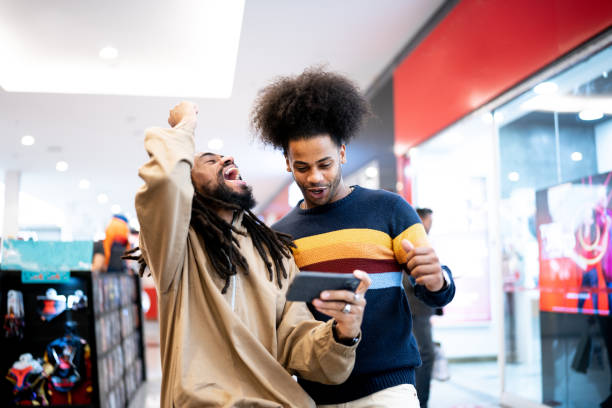 fratelli che guardano lo sport o giocano sullo smartphone al centro commerciale - spettatore foto e immagini stock