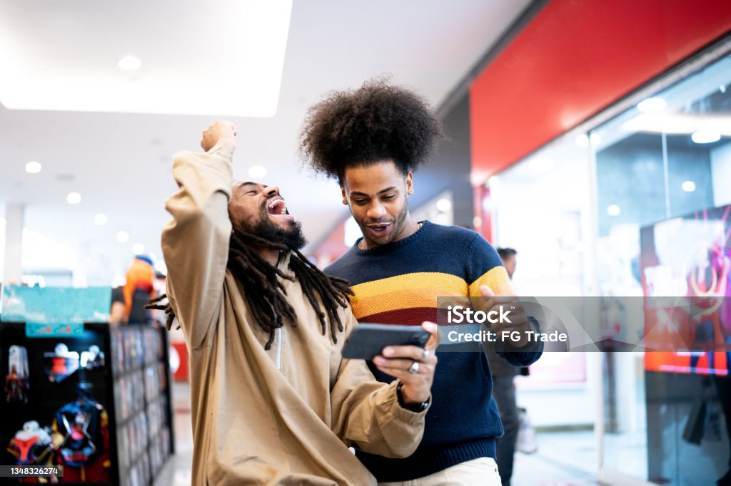 Brothers watching sports or playing on the smartphone at the mall Fan - Enthusiast Stock Photo
