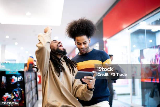 Brothers Watching Sports Or Playing On The Smartphone At The Mall Stock Photo - Download Image Now