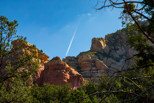 A rich blue sky has a plane's white jetstream headed down the Sedona Red Rock mountains.