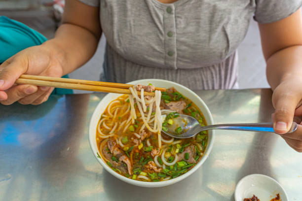 mujer comiendo bun bo hue, deliciosa comida vietnamita - long coriander fotografías e imágenes de stock
