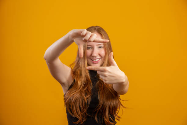 Redhead caucasian woman over yellow isolated background smiling making frame with hands and fingers with happy face. Redhead caucasian woman over yellow isolated background smiling making frame with hands and fingers with happy face. Creativity and photography concept. Film-maker or photographer. Lens vision idea. director photos stock pictures, royalty-free photos & images