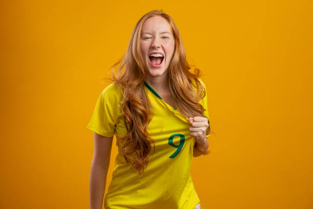 sostenitore del brasile. tifoso brasiliano di donna rossa che festeggia sul calcio, partita di calcio su sfondo giallo - celebration sport caucasian ethnic foto e immagini stock