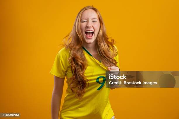 Kibic Brazylii Brazylijska Rudowłosa Fanka Świętująca Na Piłce Nożnej Mecz Piłki Nożnej Na Żółtym Tle - zdjęcia stockowe i więcej obrazów Fan