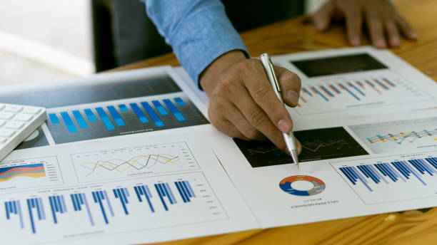 istock businessman holding pen pointing to marketing graph and working on online work concept Group of business people with financial documents and analytical calculators calculate charts while sitting at the office. 1348345193