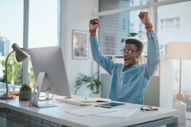 istock Shot of a young businessman cheering while using a computer at his desk in a modern office 1348346813