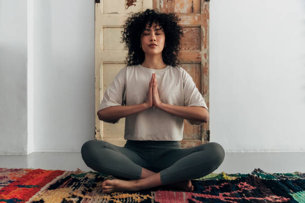 multiracial young woman meditating with hands in prayer at home - spiritualiteit stockfoto's en -beelden