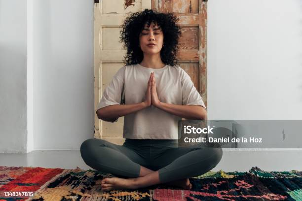 Multiracial Young Woman Meditating With Hands In Prayer At Home Stock Photo - Download Image Now