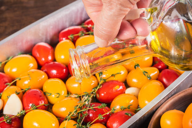 Cooking tomato confit, a woman pours oils into a baking sheet with colorful tomatoes, an elderly woman's hand with a jug of olive oil, close-up, french cuisine Cooking tomato confit, a woman pours oils into a baking sheet with colorful tomatoes, an elderly woman's hand with a jug of olive oil, close-up, french cuisine confit stock pictures, royalty-free photos & images