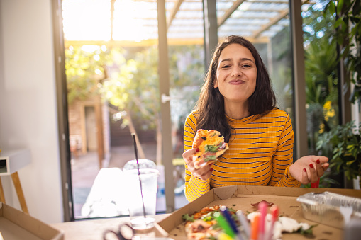 A young woman working from home, taking a break to eat a pizza for lunch.