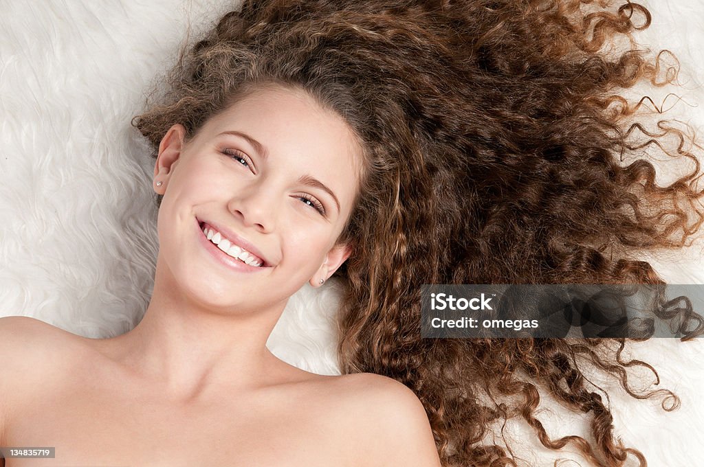 Girl with perfect curly hair lying on fur bed Closeup portrait of young emotional playful girl with perfect curly hair. Lying on white fur bed Adult Stock Photo