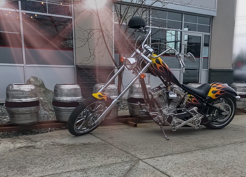 A homemade motorcycle sits in front of a restaurant. It is on display for all to see. This unique motorcycle has many characteristics and it was very intriguing  to see.