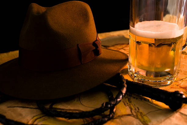 Beer stein with brown felt hat, whip and map on table.