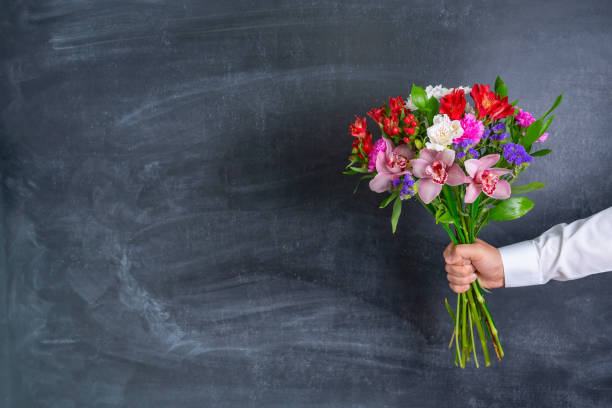 a man holding a beautiful bouquet of flowers on the background of a chalk board - öğretmenler günü stok fotoğraflar ve resimler